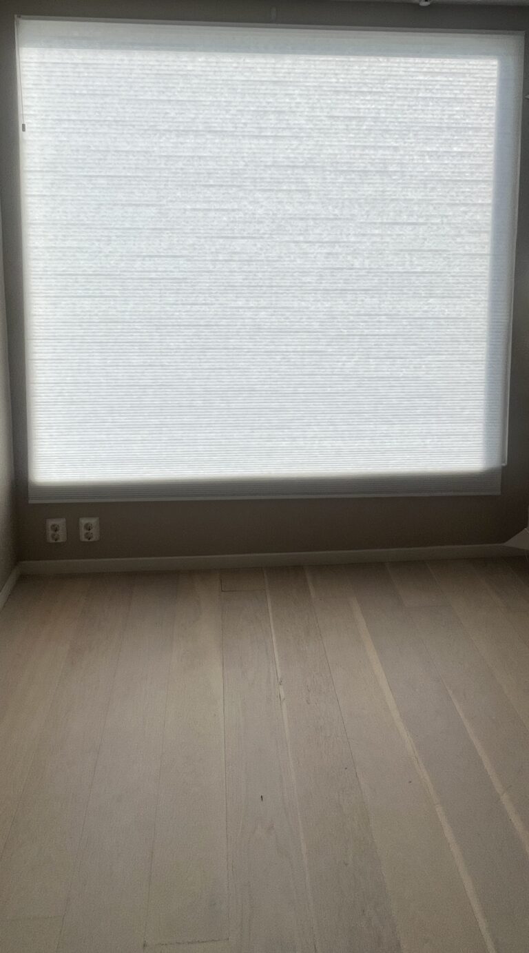 Lys plissegardin som dekker et høyt vindu