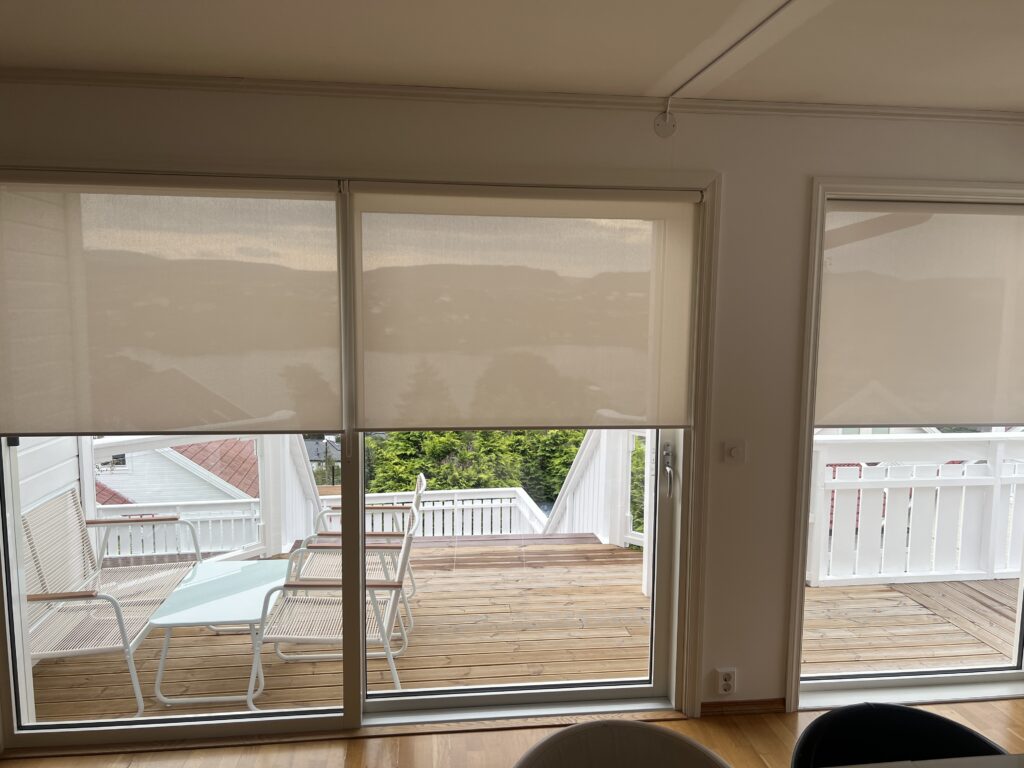 Lyse innvendige screens foran stuevinduer mot en terrasse