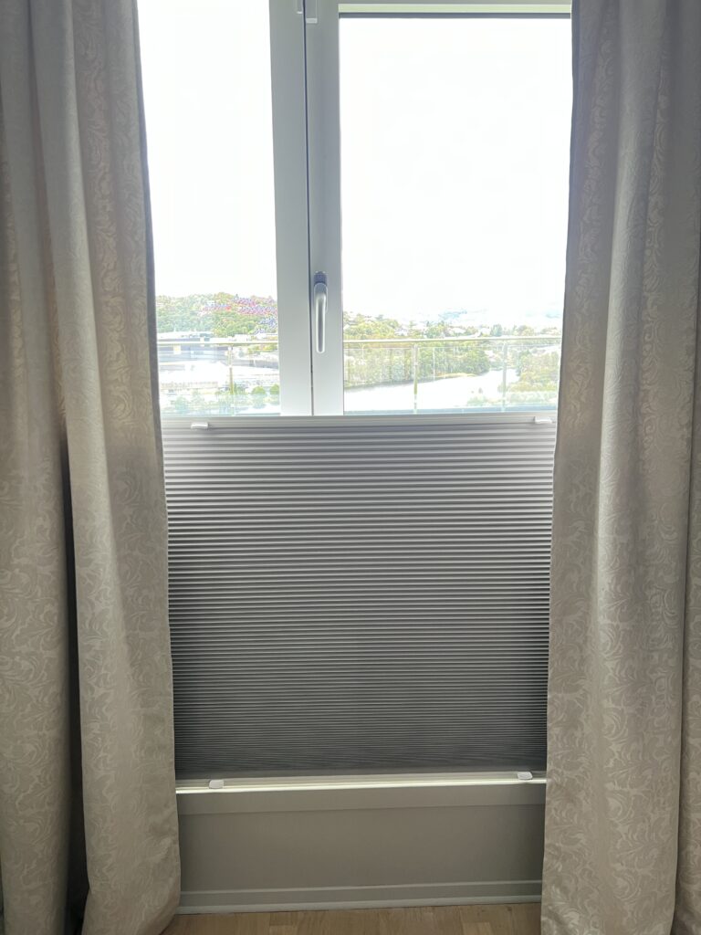 Grå plissegardin foran nedre del av et høyt vindu