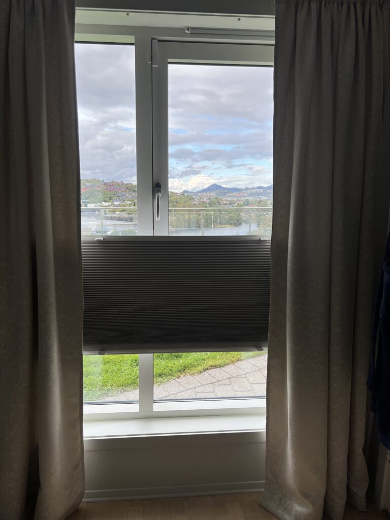 Mørk plissegardin midt på et høyt vindu