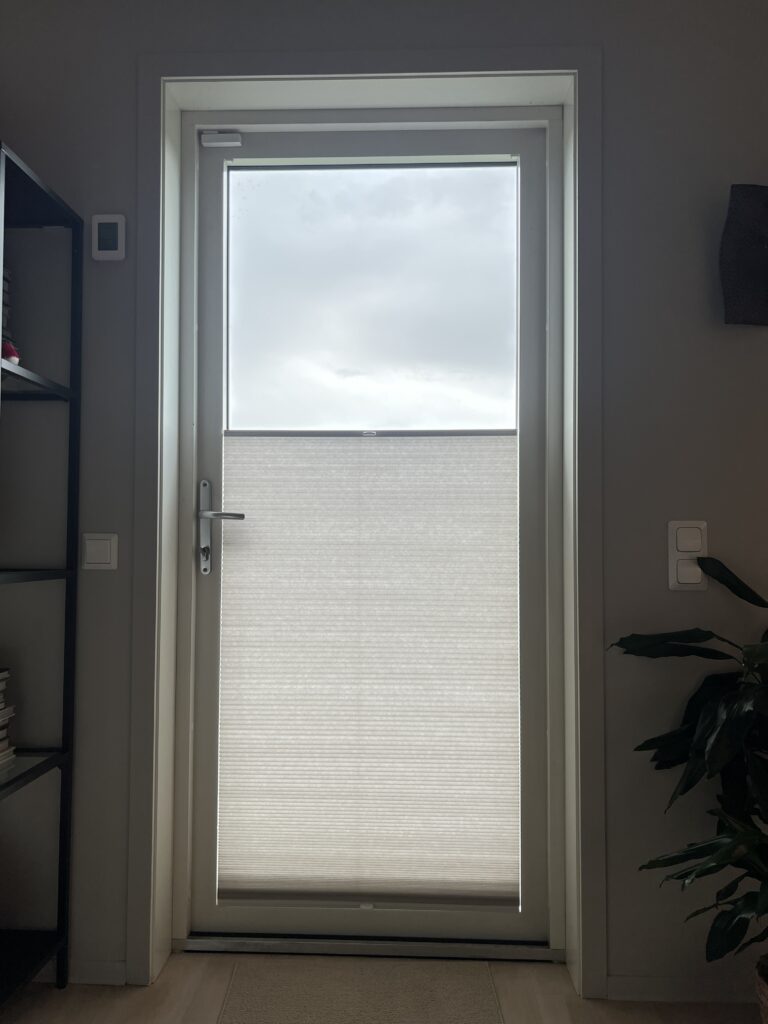 Lys plissegardin på nedre del av en balkongdør