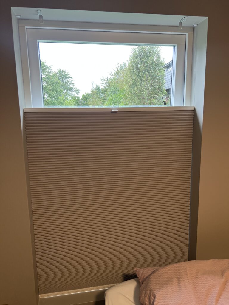 Brun plissegardin på nedre del av et soveromsvindu