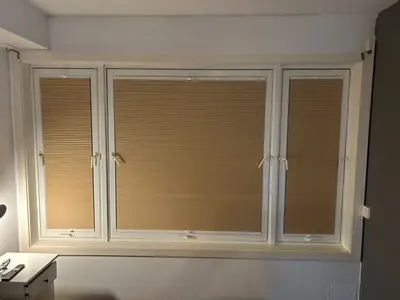 Beige plissegardiner som dekker tre vinduer i et bredt vindusparti